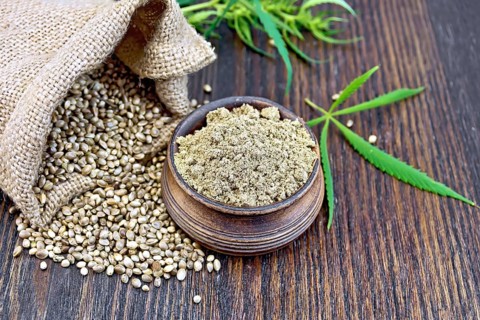 Hemp flour in a clay bowl, the grain in the bag and on the table, green cannabis leaf on a