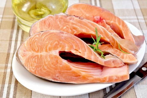 Three pieces of trout in white plate with rosemary oil in a glass decanter on a background of
