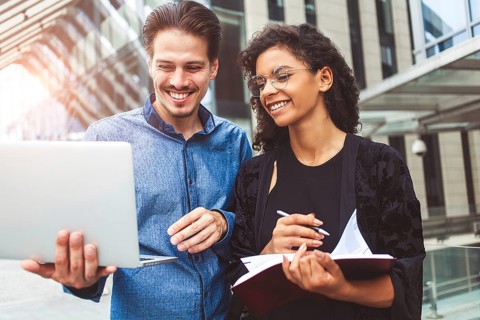 Two smiling colleagues are chatting in the street during lunch break near the building in the