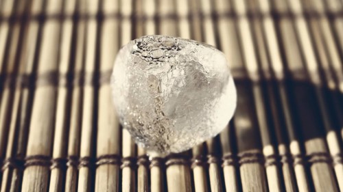 Ice cube on the wooden surface shined by the sun