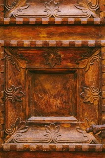 Close-up texture of brown wooden doors with raised carvings and square patterns.