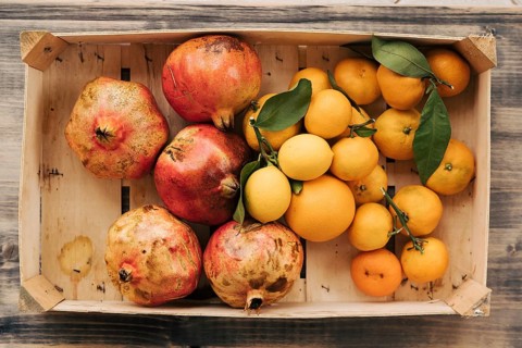 A wooden box with tangerines, lemons and pomegranates. Fruits collected in the autumn garden.