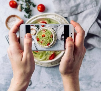 Woman hands takes top view photography of zucchini noodles salad on table with phone. Smartphone