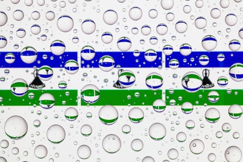 Flags of Lesotho behind a glass covered with raindrops. 3D illustration