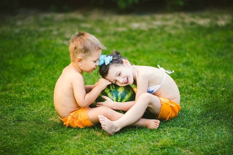 Two children, Caucasian brother and sister, sitting on green grass in backyard of house and hugging