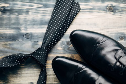 Black tie with white polka dots and men's leather shoes on a wooden background.