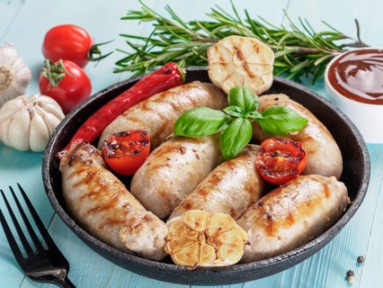 Chicken homemade sausages, sauces ketchup and vegetables and herbs on blue wooden background.