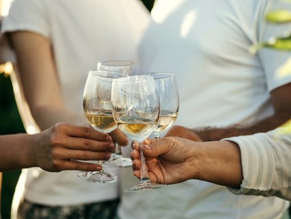 White wine glasses in hands. Four unrecognizable people clang glasses together outdoors