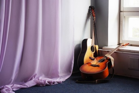 Two acoustic guitar next the window and drapery