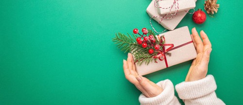 Christmas or New Year celebration green paper festive background with female hands holding wrapped