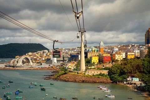 Cable cars over a city with colorful buildings by the waterfront under a cloudy sky, cable car,