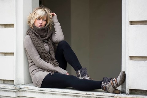 Attractive blonde young woman sitting on window sill, wearing winter clothes