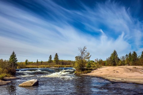 Foam water rapids on the smooth stones of the Winnipeg River. Thin cirrus clouds. Trend of travel