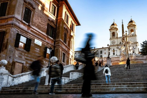 People in motion on the steps of the Spanish Steps in front of historic buildings under a blue sky,