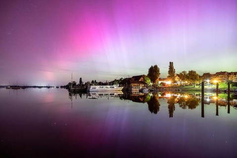 A calm lake at night, surrounded by shining auroras and reflecting houses, harbour, Allensbach,