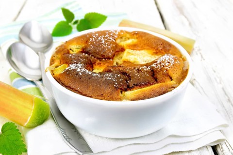 Pie clafouti with rhubarb in the bowl, mint and rhubarb stems on a napkin on wooden plank