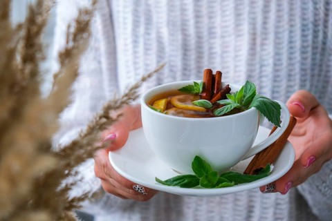 Female hands on sweater holding tea with lemon, cinnamon sticks and mint leaves. Hot drink. Healthy