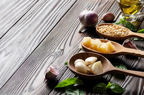 Closeup view at wooden spoons with food ingredients for genovese pesto sauce on kitchen table