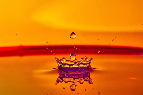 A falling drop of water creates an impressive crown on an orange-coloured surface, high-speed