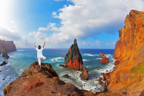 The woman ashore in a white suit for yoga carries out a pose Tree. Atlantic storms. Colorful