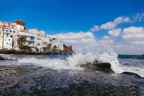 Sea wave with splashes and white houses near seashore at geek island
