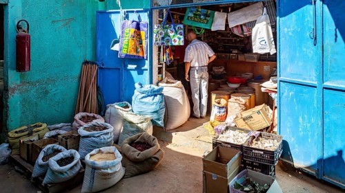 A man in a small shop full of colourful sacks and goods in bright sunshine, Small shop in