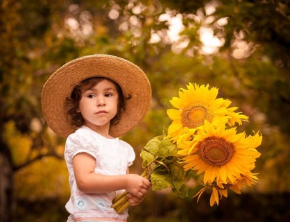 Little girl with sunflowers in a stetson on the garden