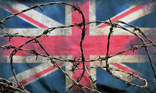 Barbed wire in front of an old stained dirty union jack british flag with dark crumpled edges
