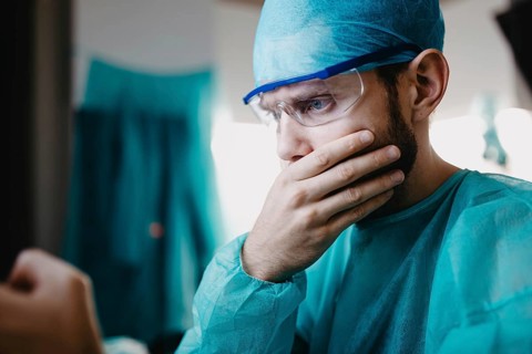A surgeon in blue attire, appearing concerned with a hand on the mouth