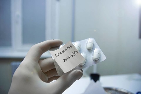 A gloved hand holds a pill package labeled 'Coronavirus 2019-nCoV' in a laboratory