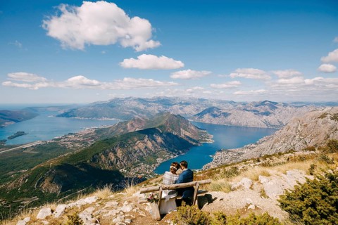 Bride and groom are sitting on a bench and looking at the Kotor bay. Excellent view from the