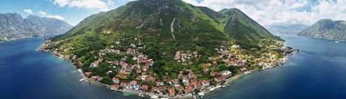 Old houses with red roofs on the seashore on the slope of a green mountain. Montenegro. Drone.