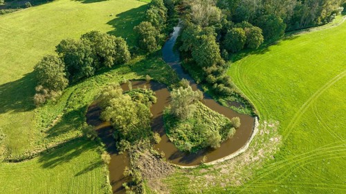 Aerial view of a beautiful green landscape with a small river flowing through. It is in the eastern
