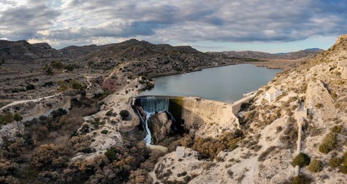 A drone view of the Elche Reservoir and dam wall with waterfall and surrounding semi-desert