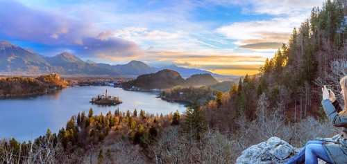 Panorama with the lake Bled under a colorful winter sky at sunrise and a young woman enjoys the