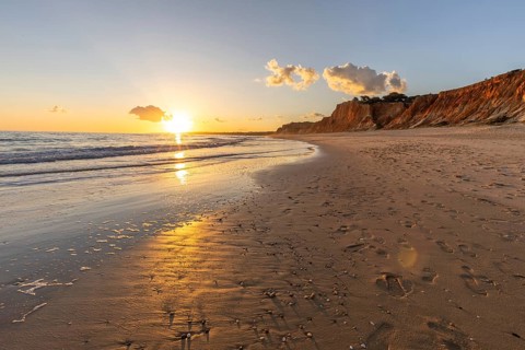 Beautiful sandy beach with red rocks and cliffs. Twilight at sunset with shallow waves on the