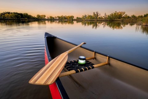 Red canoe with a wooden paddle and lantern on a lake at dusk, fall scenery, wide angle view
