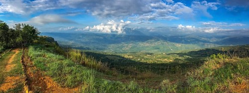 Panorama over the cliffs into a green valley and mountains in sun and shadow, blue sky and white
