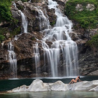 Professional model in elegant pose on a rocky island in front of an impressive waterfall, Aesthetic