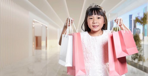 Asian girl wearing a princess tiara is smiling and holding shopping bags inside of a mall