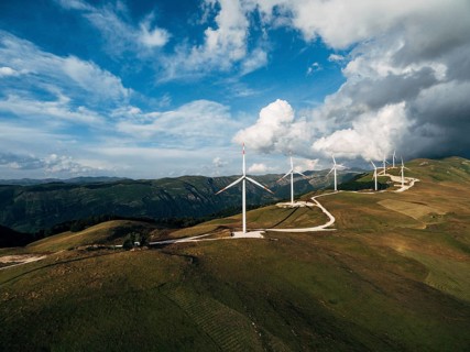 The prospect of a number of high industrial wind turbines on the hill, against the blue sky and