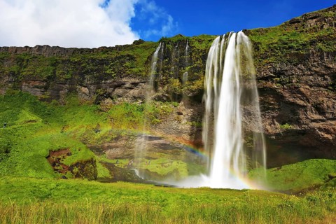 Sunny day in July. Seljalandsfoss waterfall in Iceland. Large rainbow decorates a drop of water
