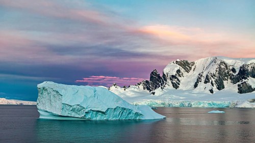 Iceberg floating in the sea in front of a snow-covered mountain backdrop at sunset, icebergs in the