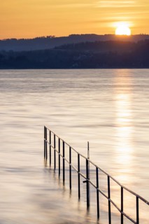 Rising sun over calm lake, railing extends into the water, lido, Litzelstetten, Lake Constance,
