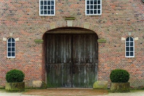 Large wooden gate in a symmetrical brick building with trimmed shrubs, vreden, münsterland, North