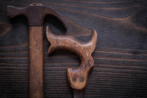 Rusted messy handsaw and claw hammer on vintage wooden background