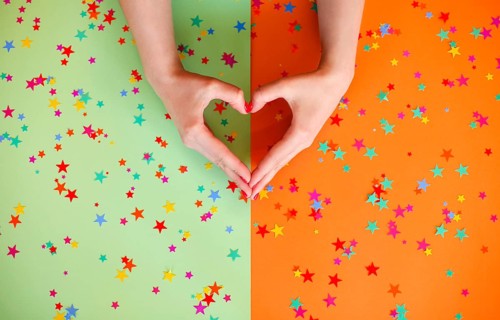 Top view of anonymous female with hands in shape of heart on two colored background with confetti
