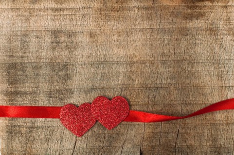 Red ribbon tape and hearts on wooden background