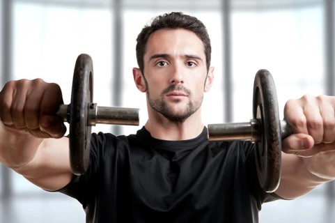 Personal Trainer doing front dumbell raises for training his deltoids in a brown background