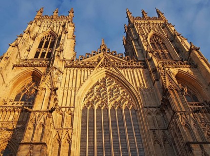 A front view of the towers at the entrance to york minster in sunlight against a blue cloudy sky